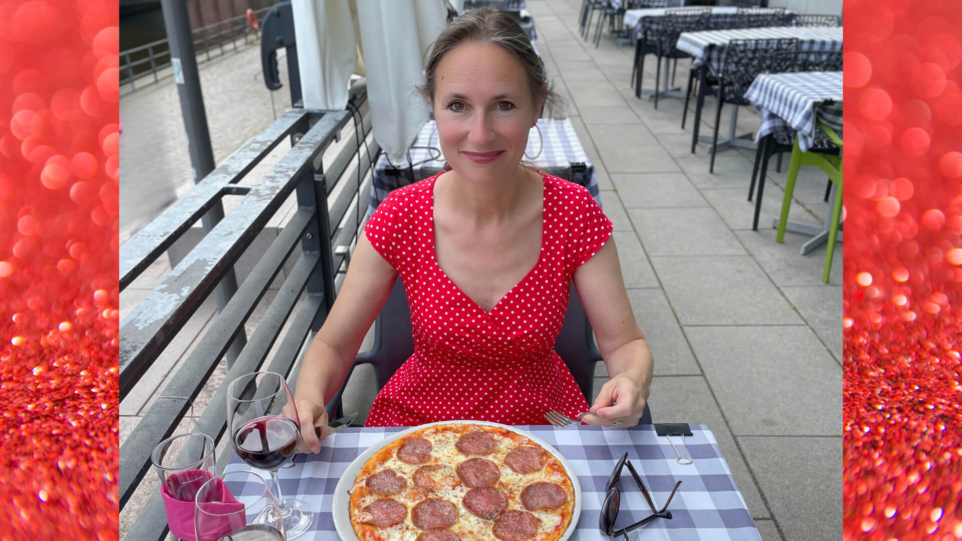 Frau im roten Kleid isst Pizza auf einer Restaurant-Terrasse