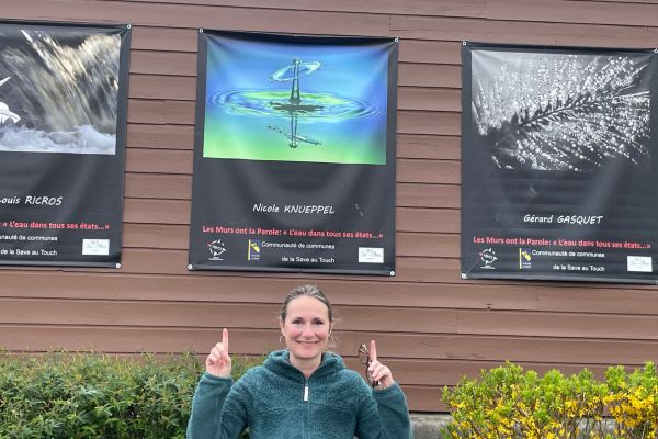 Frau zeigt auf ein Plakat mit einer Fotografie auf einer Hauswand hinter ihr